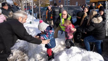 Parents and their children are loaded onto a warming bus as they wait for news after a bus crashed into a day care center in Laval, Quebec, on February 8, 2023.