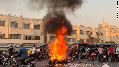 A picture obtained by AFP outside Iran, shows people gathering next to a burning motorcycle in the capital Tehran on October 8, 2022. 