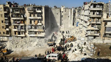 Syrian soldiers look on as rescuers use heavy machinery to sift through the rubble of a collapsed building in the northern city of Aleppo. 