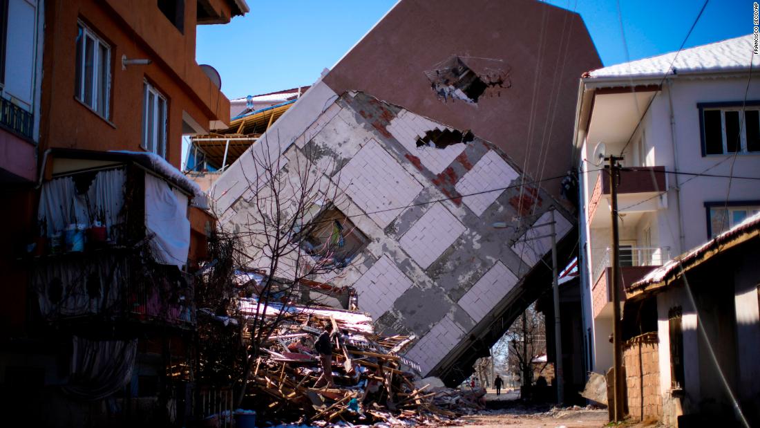 A man walks near a building that toppled over onto a neighboring structure in Golbasi, Turkey, on February 13.