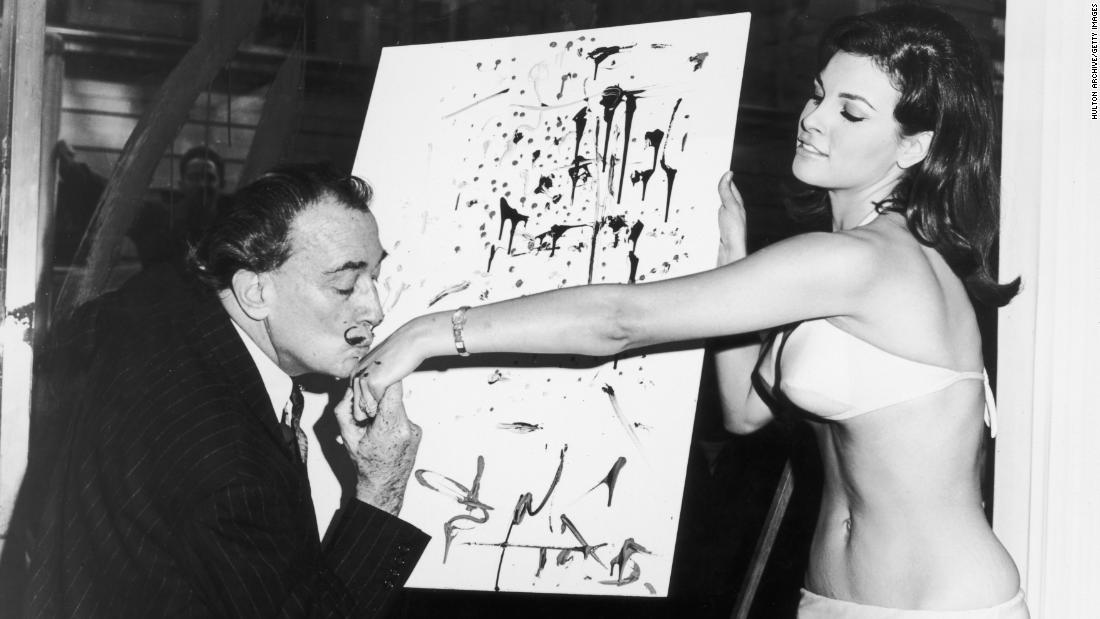 Artist Salvador Dali kisses Welch&#39;s hand in front of an abstract portrait of her circa 1965.