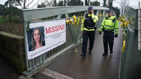 Police officers walk past a missing person appeal poster for Nicola Bulley.