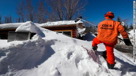 BIG BEAR LAKE, CA - MARCH 03: A Cal Fire Fenner Canyon fire crew inmate drags snow off the roof of a residence at a Big Bear Lake trailer park as the area digs out following successive storms which blanketed San Bernardino Mountain communities on Friday, March 3, 2023 in Big Bear Lake, CA. (Brian van der Brug / Los Angeles Times via Getty Images)