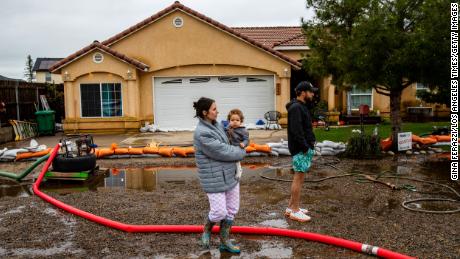 Madisyn Liles holds Luka, 1, and watches with her husband Keylan as two pumps work Wednesday to remove floodwater from their home after a night of heavy rain in Woodlake, California. 