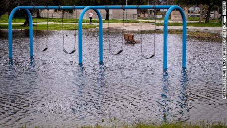 A person walks past a flooded playground section in Huntington Beach Monday, March 20, 2023.
