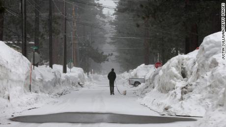 A man walks his dog on a snow covered street as snow begins to fall Tuesday in South Lake Tahoe, California. 