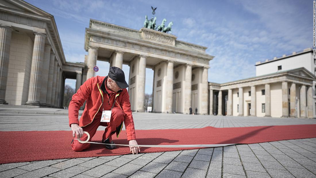 A man fastens a red carpet in front of the Brandenburg Gate.