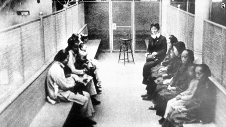 In this file photo from the 1920s, a group of Chinese and Japanese women and children wait to be processed as they are held in a wire mesh enclosure at internment barracks in Angel Island, California. As a result of the Chinese Exclusion Act and subsequent restrictions, immigrants were detained for extended periods of time there and faced the possibility of deportation.