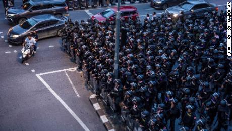 Motorists ride past riot police in Bangkok on October 15, 2020, after Thailand issued an emergency decree following an anti-government rally the previous day. 