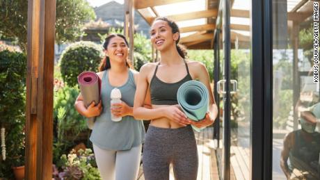 Fitness, yoga women walking to class with training gear and water bottle for sports teamwork at wellness center. Pilates, workout and healthy people or friends talking of holistic exercise in nature