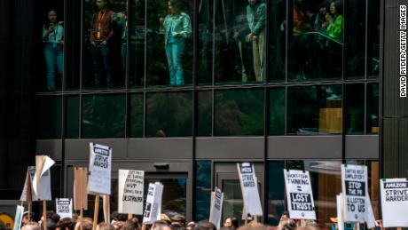 People watch from inside Amazon&#39;s Day One building as Amazon workers hold signs during a walkout event at the company&#39;s headquarters on May 31, 2023 in Seattle, Washington. The protest action was organized to call attention to return to office requirements, in addition to recent layoffs and climate change issues. 