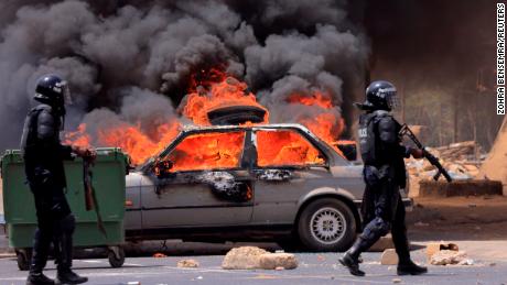 Riot police officers walk near a car set on fire during clashes between supporters of Senegalese opposition leader Ousmane Sonko and security forces after Sonko was sentenced to prison in Dakar Senegal June 1, 2023.