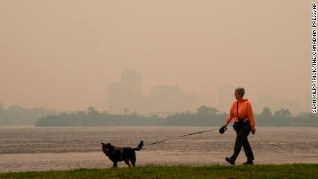 A woman walks her dog Tuesday along the Ottawa River in Ottawa as smoke obscures Gatineau, Quebec.
