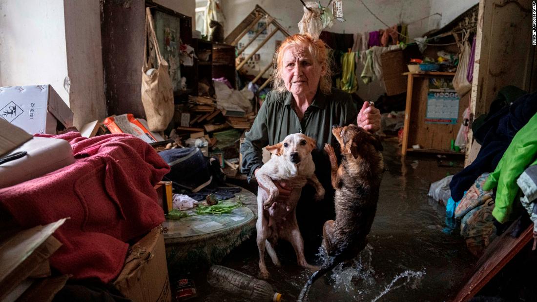 Local resident Tetiana holds her pets, Tsatsa and Chunya, as she stands inside her flooded house after the destruction of the dam.