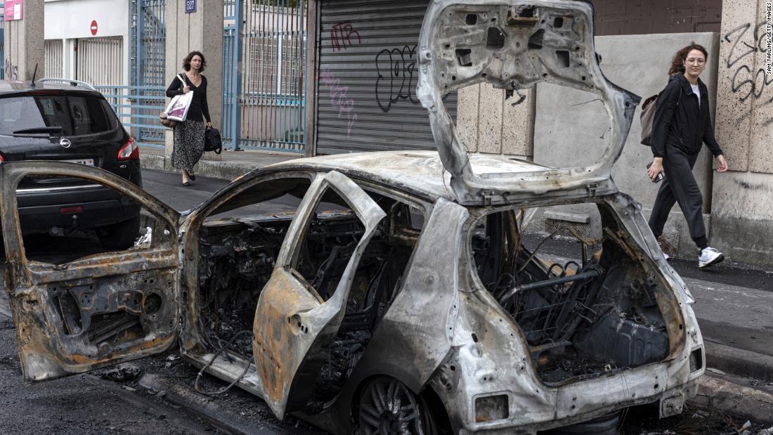 A passerby looks at the scorched remains of a car set on fire during protests in Colombes, France, on July 1.