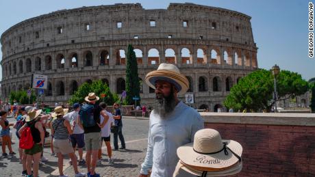 A street vendor walks with hats in front of the Colosseum in Rome, Monday, July 17, 2023.