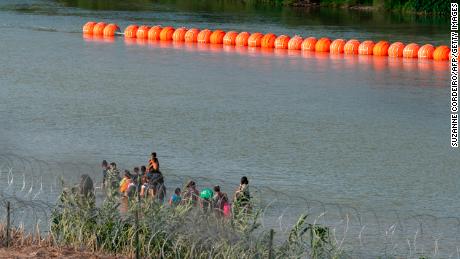 Migrants walk by a string of buoys placed along the Rio Grande border with Mexico in Eagle Pass, Texas, on July 16.