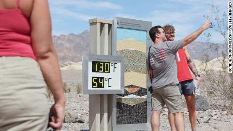Tourists stand next to an unofficial heat reading at Furnace Creek Visitor Center during a heat wave in Death Valley National Park.