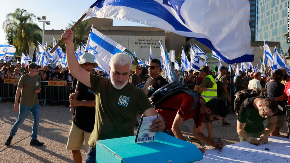 An Israeli military reservist in Tel Aviv waves a national flag as he drops a signed declaration in a box, announcing the suspension of his voluntary reserve duty, on Wednesday, July 19. He was protesting the government&#39;s judicial overhaul plans.