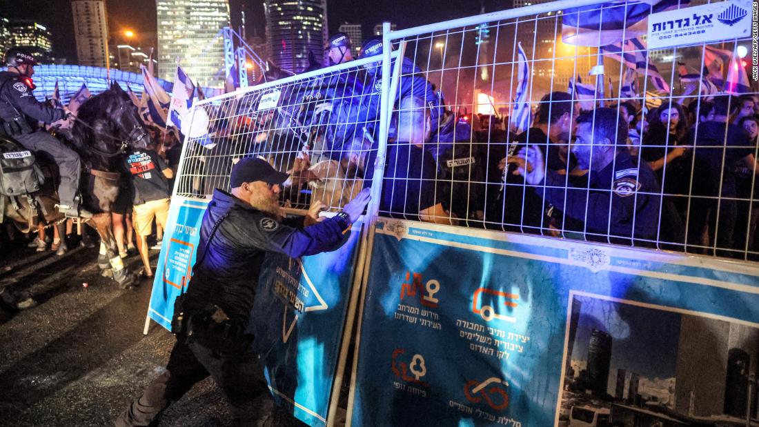 An Israeli policeman stands behind a metal fence being shoved by demonstrators in Tel Aviv on July 24.