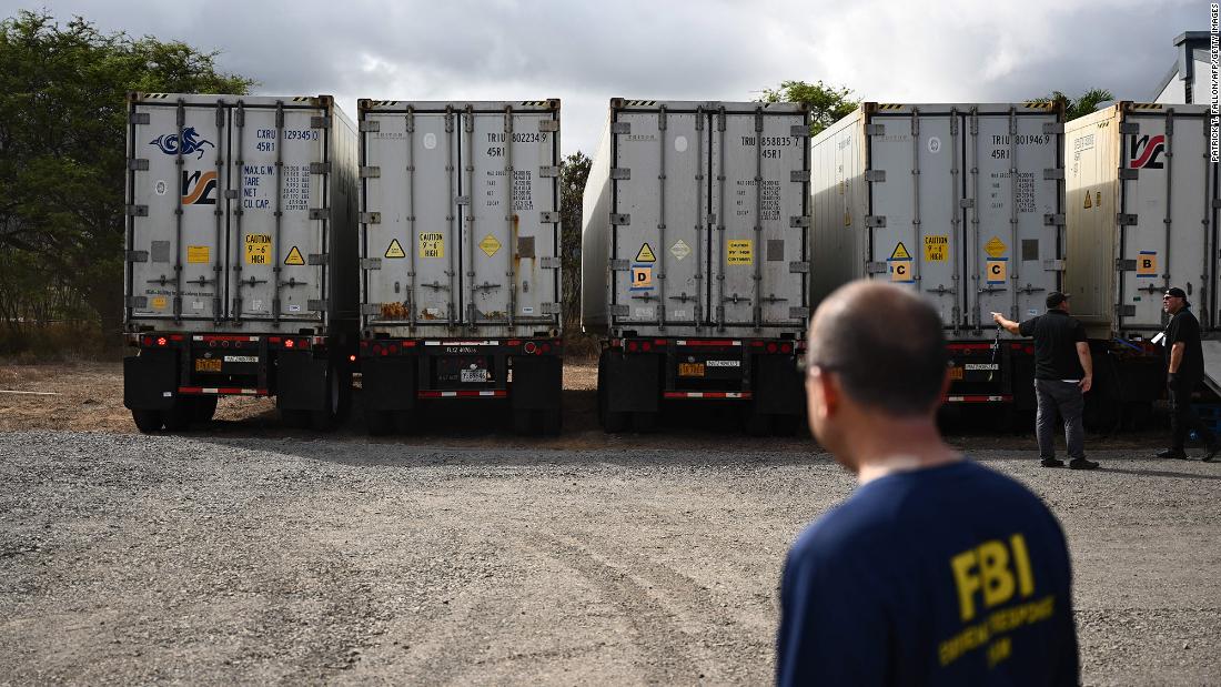 An FBI agent watches as two additional refrigerated storage containers arrive next to the Maui Police Forensic Facility where human remains were being stored in Wailuku, Hawaii, on Monday, August 14.
