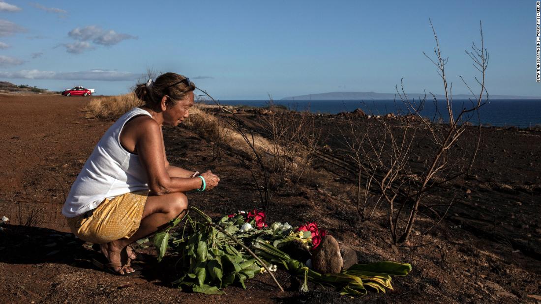 A woman lays down flowers and prays on a hillside overlooking the rubble of Lahaina on August 16.