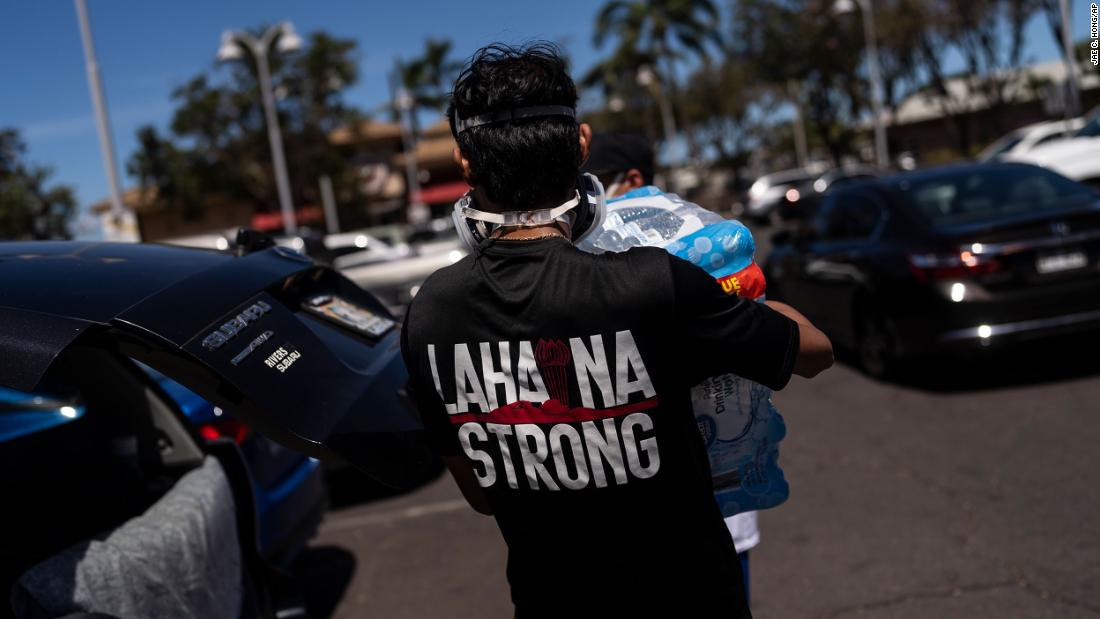 Ken Alba carries a bag of ice at a food and supply distribution center that was set up in the parking lot of a Lahaina shopping mall on Thursday, August 17.