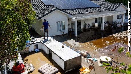 CATHEDRAL CITY, CA  - AUGUST 21, 2023: Nick Rodriguez stands on top of an outdoor barbecue seating area  at his brother&#39;s flooded backyard from the remnants of tropical storm Hilary on August 21, 2023 in Cathedral City, California. The inside of the house has 18 inches of flood water. &quot;The water came into the house about midnight full throttle, Rick Figueroa said. He and his family hunkered down in one room until sunrise. Unable to escape out their front door Figueroa&#39;s wife Dawn and daughter Ella escaped over a neighbor&#39;s back wall Monday morning.(Gina Ferazzi / Los Angeles Times via Getty Images)