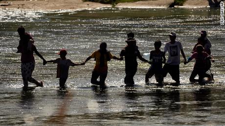 Migrants join hands as they cross the Rio Grande from Mexico into the US, on Thursday, Sept. 21, 2023, in Eagle Pass, Texas.