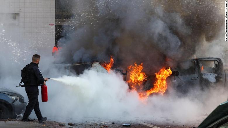 A member of Israeli security forces tries to extinguish fire on cars following a rocket attack from the Gaza Strip in Ashkelon, southern Israel.