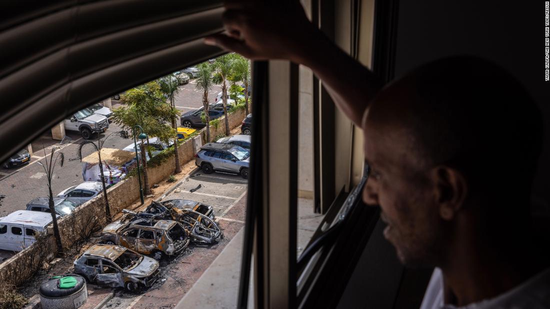 From the window of his family&#39;s apartment, a man surveys damage from a rocket that struck a parking lot in Ashkelon on October 7.