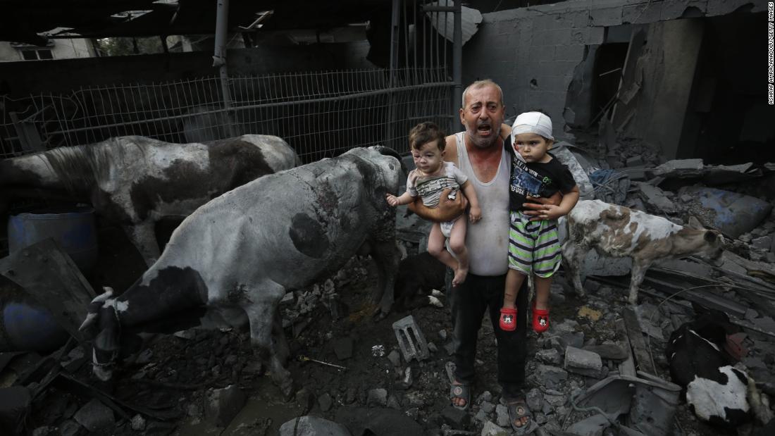 A man holds wounded children near livestock animals amid heavily damaged buildings, following Israeli attacks at Nuseirat Refugee Camp in Gaza City, on Sunday, October 29.