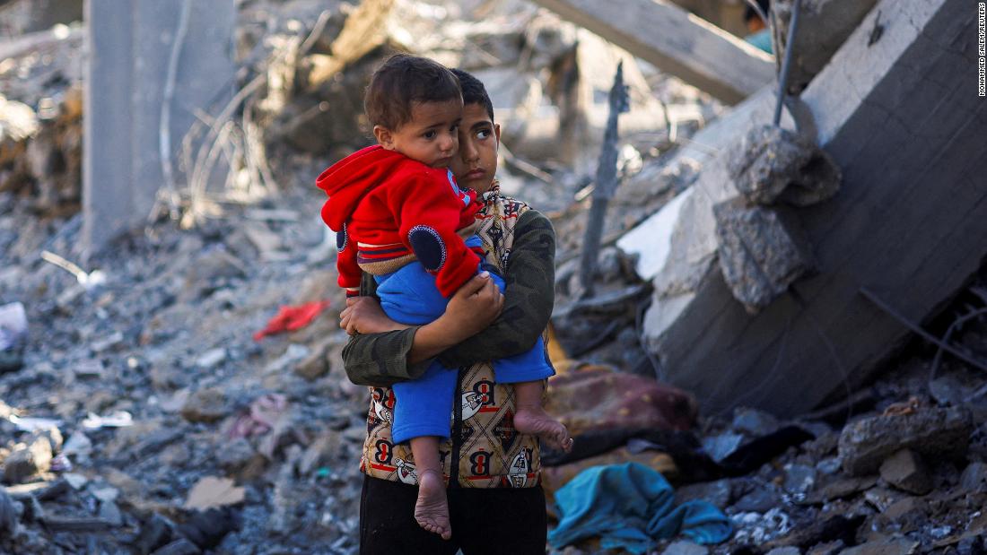 A Palestinian boy carrying a baby stands at a site of Israeli strikes in Rafah, southern Gaza, on December 4.