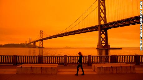 TOPSHOT - A woman walks along The Embarcadero under an orange smoke-filled sky in San Francisco, California on September 9, 2020. - More than 300,000 acres are burning across the northwestern state including 35 major wildfires, with at least five towns &quot;substantially destroyed&quot; and mass evacuations taking place. (Photo by Brittany Hosea-Small / AFP) (Photo by BRITTANY HOSEA-SMALL/AFP via Getty Images)