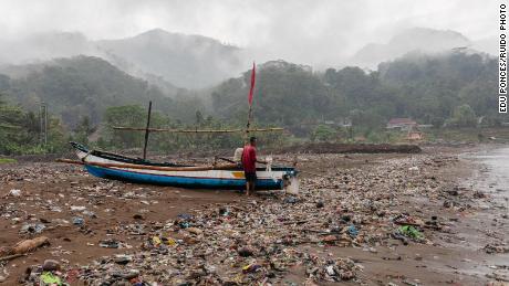 A local fisherman performs maintenance on his boat at Loji Beach, West Java, surrounded by garbage.
